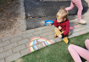Dzieci rysują na chodniku kredą.