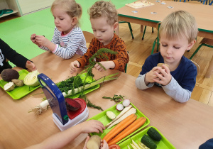 Dzieci przy stoliku oglądają warzywa