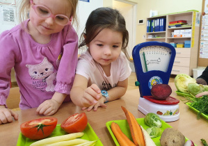 Dzieci przy stoliku oglądają warzywa