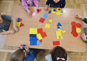 Dzieci przy stolikach układają kompozycje z figur geometrycznych