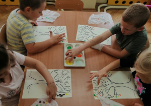 Dzieci przy stoliku malują jesienne drzewa
