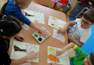Dzieci przy stoliku malują jesienne drzewa