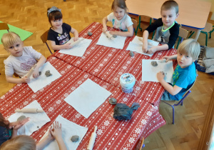 Dzieci siedzą przy stoliku i lepią z gliny